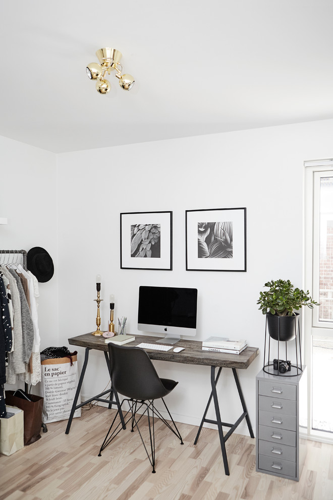 Inredning av ett minimalistiskt arbetsrum, med vita väggar, ljust trägolv och ett fristående skrivbord