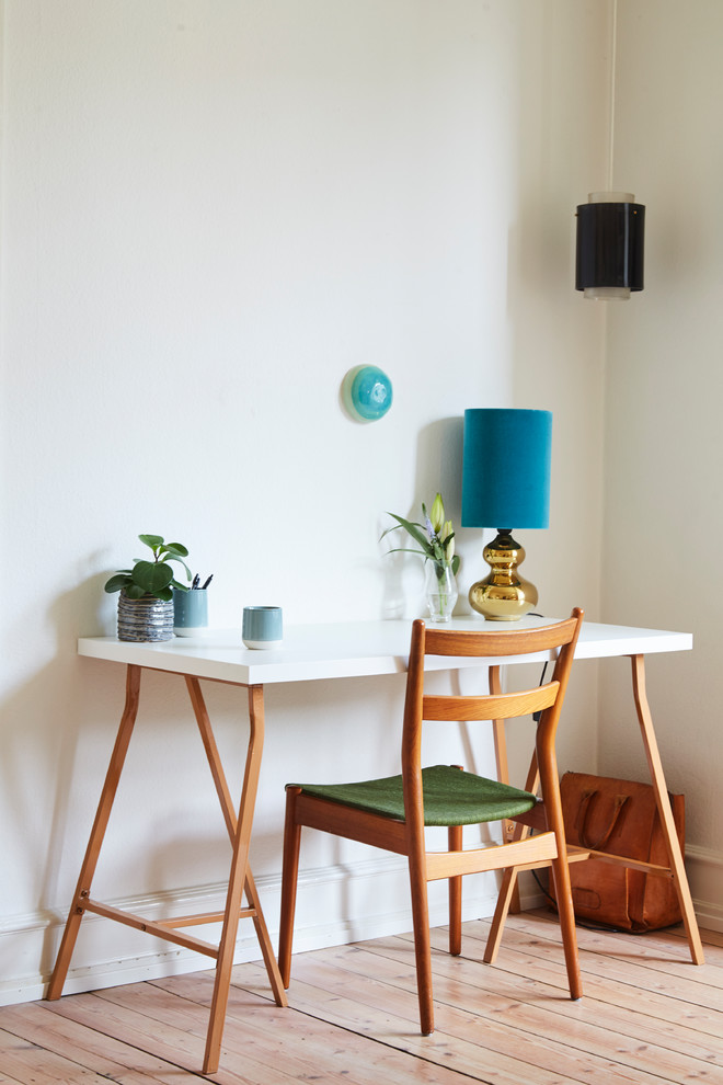 Modelo de despacho retro pequeño sin chimenea con paredes blancas, suelo de madera clara, escritorio independiente y suelo beige