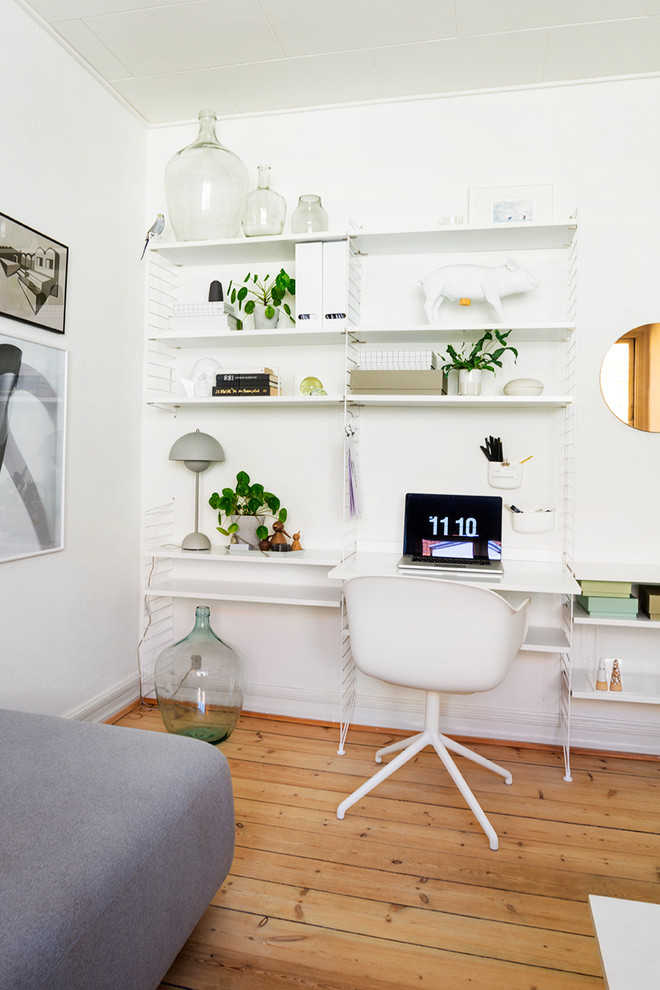 Foto på ett nordiskt arbetsrum, med vita väggar, mellanmörkt trägolv och ett fristående skrivbord