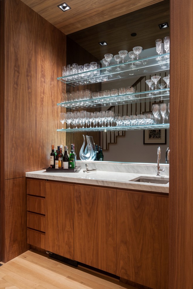 Esempio di un piccolo angolo bar moderno con lavello sottopiano, ante lisce, ante in legno bruno, top in marmo, paraspruzzi nero, pavimento in legno massello medio, pavimento marrone e paraspruzzi a specchio