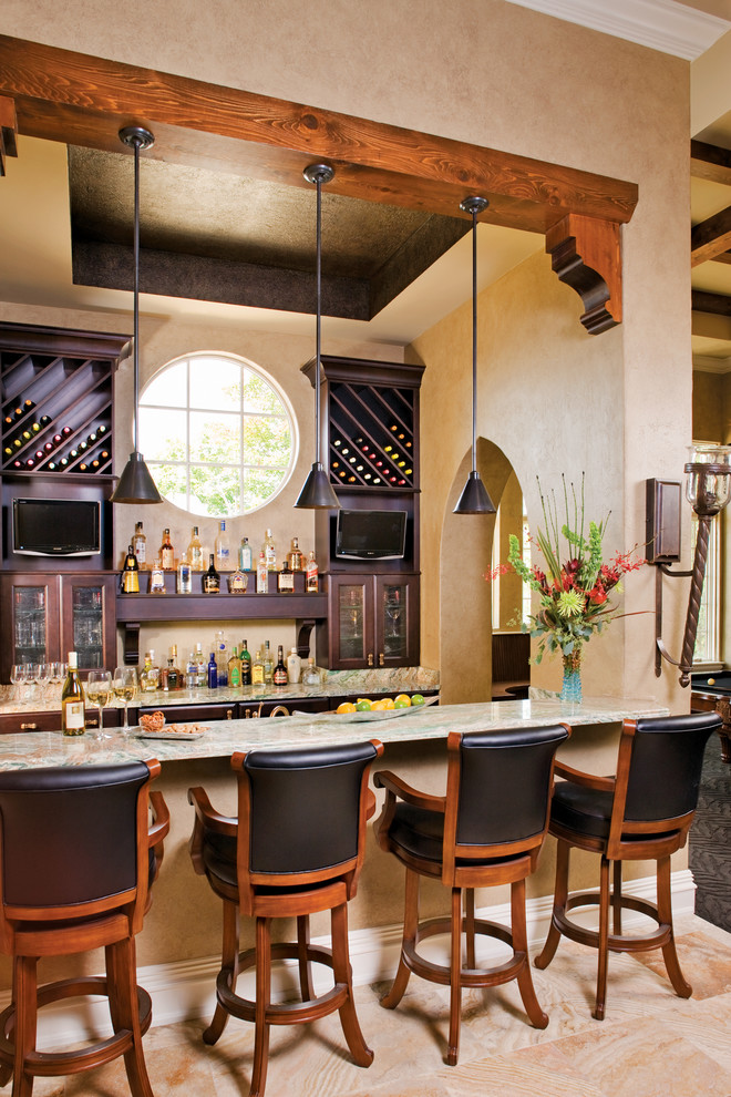 Стильный дизайн: большой параллельный домашний бар в средиземноморском стиле с барной стойкой, стеклянными фасадами, темными деревянными фасадами, гранитной столешницей и полом из известняка - последний тренд