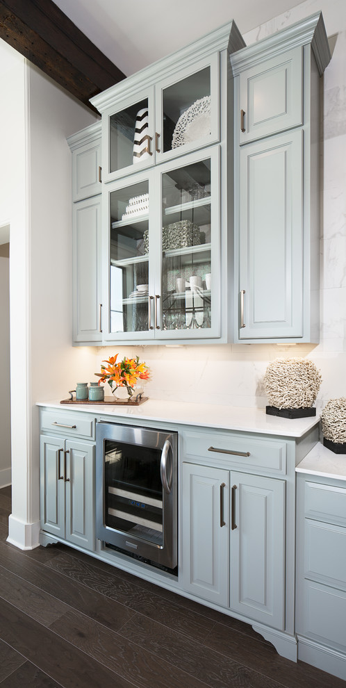 Mid-sized transitional single-wall medium tone wood floor home bar photo in New Orleans with white backsplash, raised-panel cabinets, blue cabinets, marble countertops and white countertops
