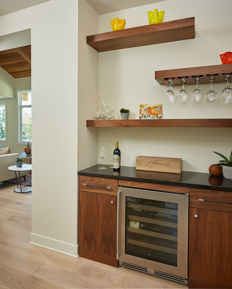 This is an example of a rural single-wall home bar with flat-panel cabinets, medium wood cabinets, white splashback, light hardwood flooring and brown floors.