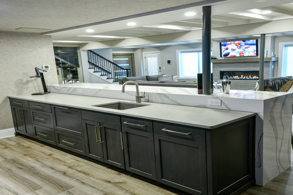 Seated home bar - large contemporary single-wall vinyl floor and beige floor seated home bar idea in Cleveland with an undermount sink, shaker cabinets, dark wood cabinets, quartz countertops, gray backsplash and gray countertops