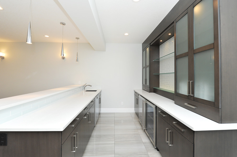 This is an example of a medium sized modern galley wet bar in Calgary with a submerged sink, flat-panel cabinets, dark wood cabinets, composite countertops, porcelain flooring, grey floors and white worktops.