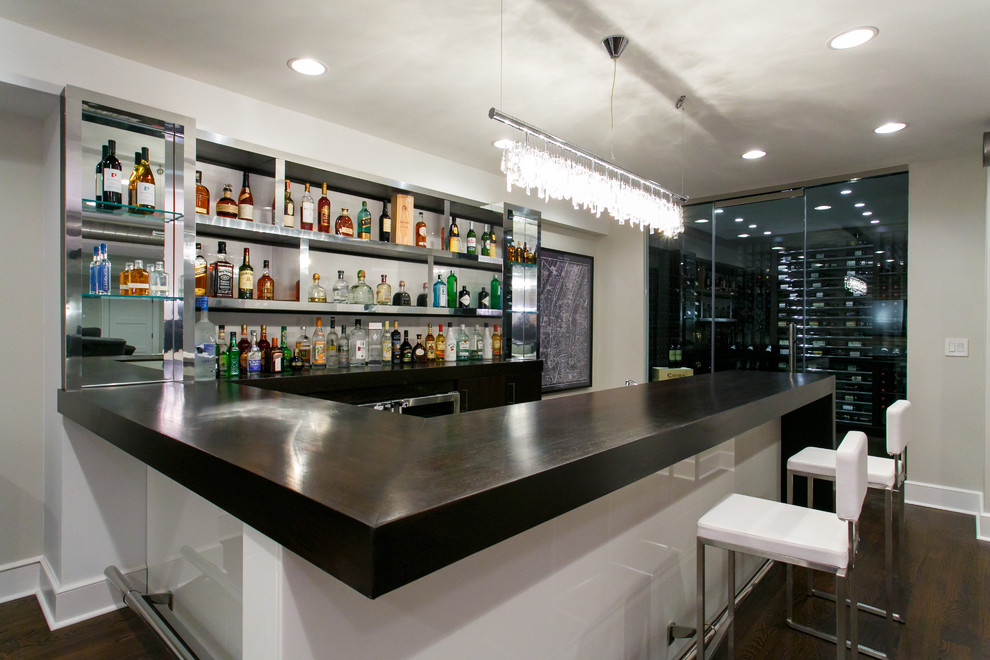 Modelo de bar en casa con barra de bar en U actual grande con encimera de vidrio, salpicadero blanco y suelo de madera oscura