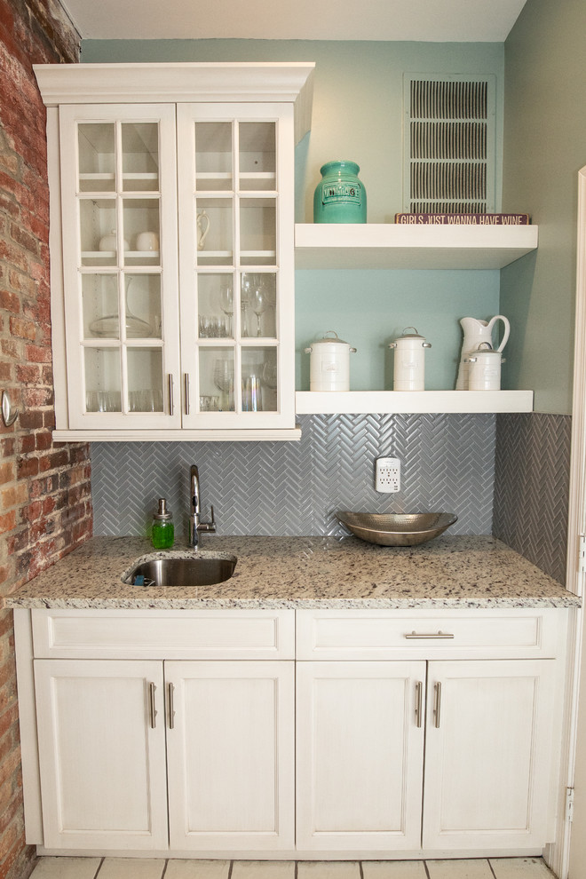 Photo of a small galley wet bar in DC Metro with a submerged sink, shaker cabinets, white cabinets, granite worktops, grey splashback, glass tiled splashback and beige worktops.