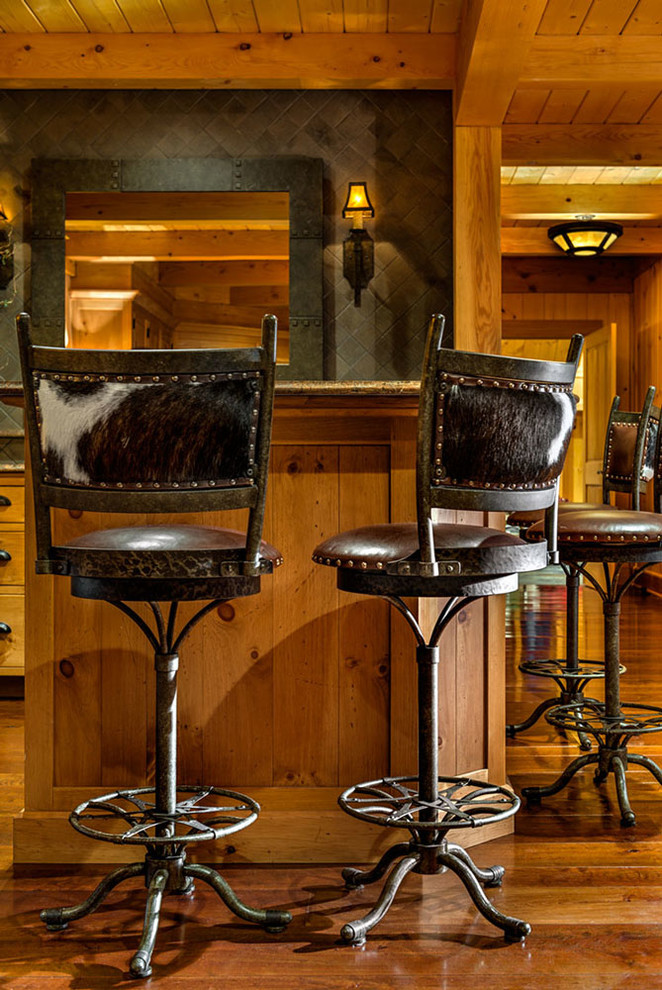 Cette image montre un grand bar de salon chalet en bois brun avec des tabourets, un placard avec porte à panneau encastré, un plan de travail en granite, une crédence grise et une crédence en céramique.