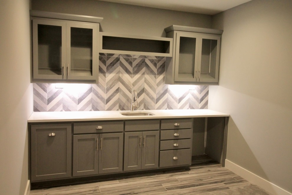 This is an example of a medium sized traditional single-wall wet bar in Kansas City with a submerged sink, shaker cabinets, grey cabinets, engineered stone countertops, grey splashback, ceramic splashback, ceramic flooring and grey floors.