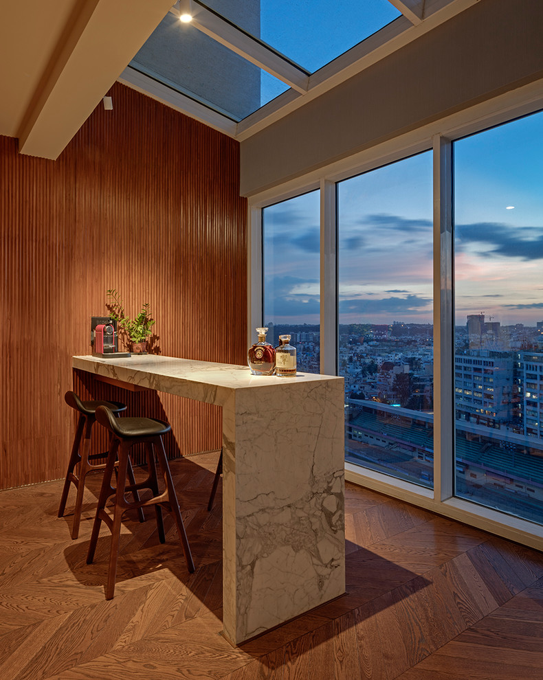Cette image montre un bar de salon design avec des tabourets, plan de travail en marbre, un sol en bois brun et un plan de travail blanc.