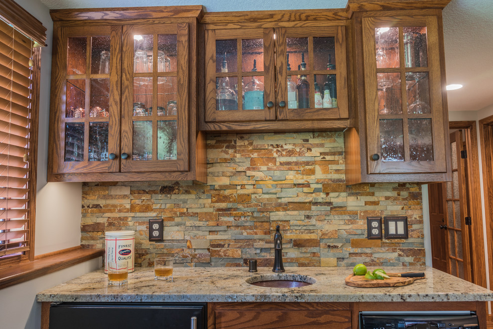 Inspiration for a medium sized traditional single-wall wet bar in Minneapolis with no sink, recessed-panel cabinets, medium wood cabinets, granite worktops, multi-coloured splashback, stone tiled splashback, cork flooring and brown floors.