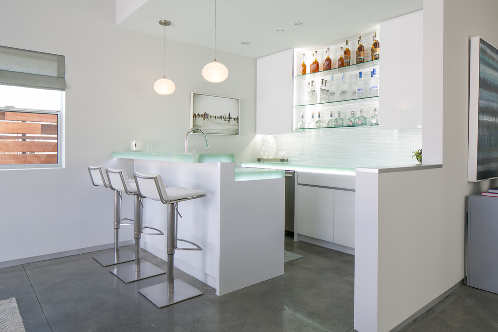 Zweizeilige, Mittelgroße Moderne Hausbar mit flächenbündigen Schrankfronten, weißen Schränken, Glas-Arbeitsplatte, Küchenrückwand in Weiß und Betonboden in Orange County
