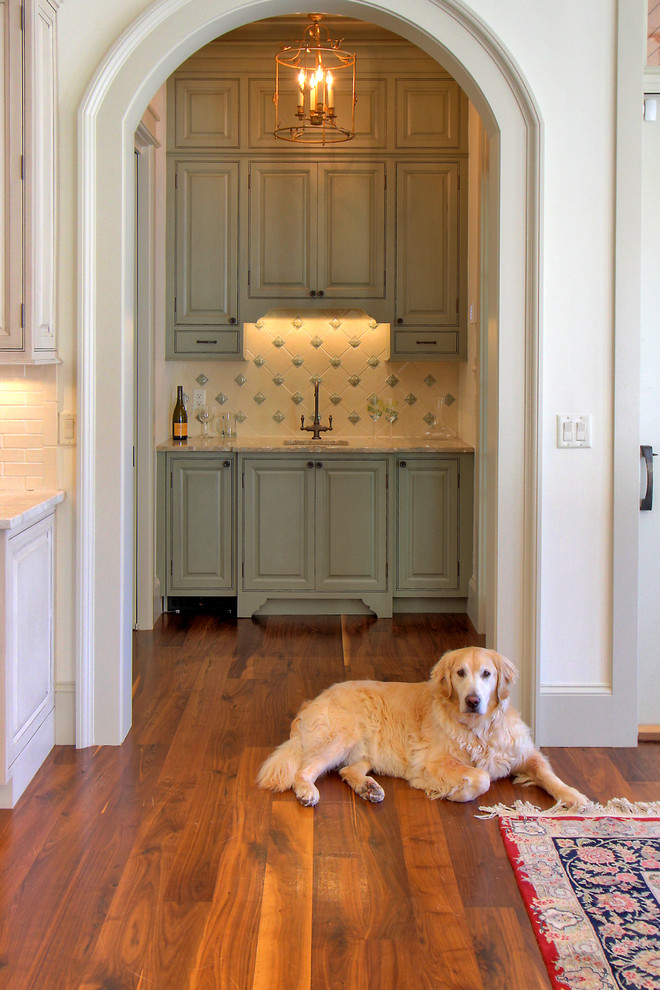 Exempel på en klassisk hemmabar med vask, med luckor med upphöjd panel, gröna skåp, beige stänkskydd och mörkt trägolv