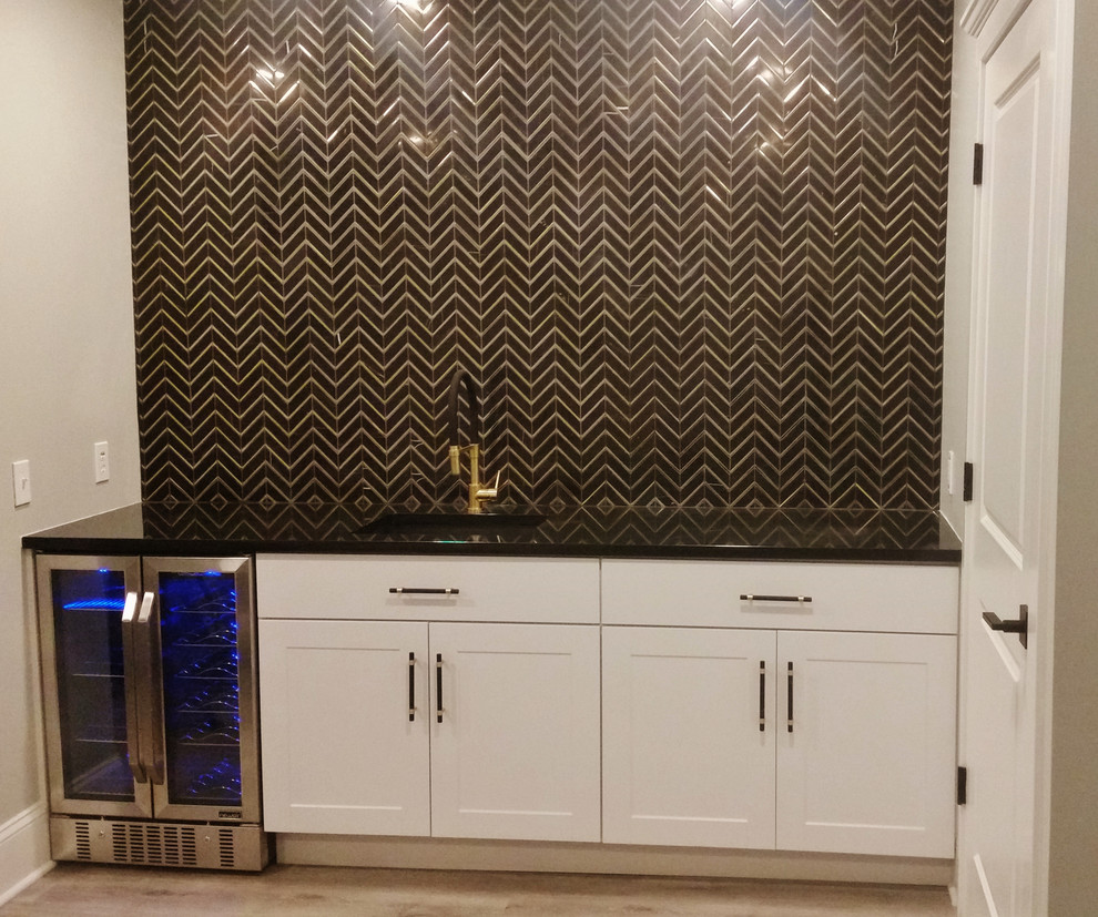 Photo of a contemporary galley wet bar in Chicago with a submerged sink, shaker cabinets, white cabinets, granite worktops, black splashback, stone tiled splashback, vinyl flooring, grey floors and black worktops.