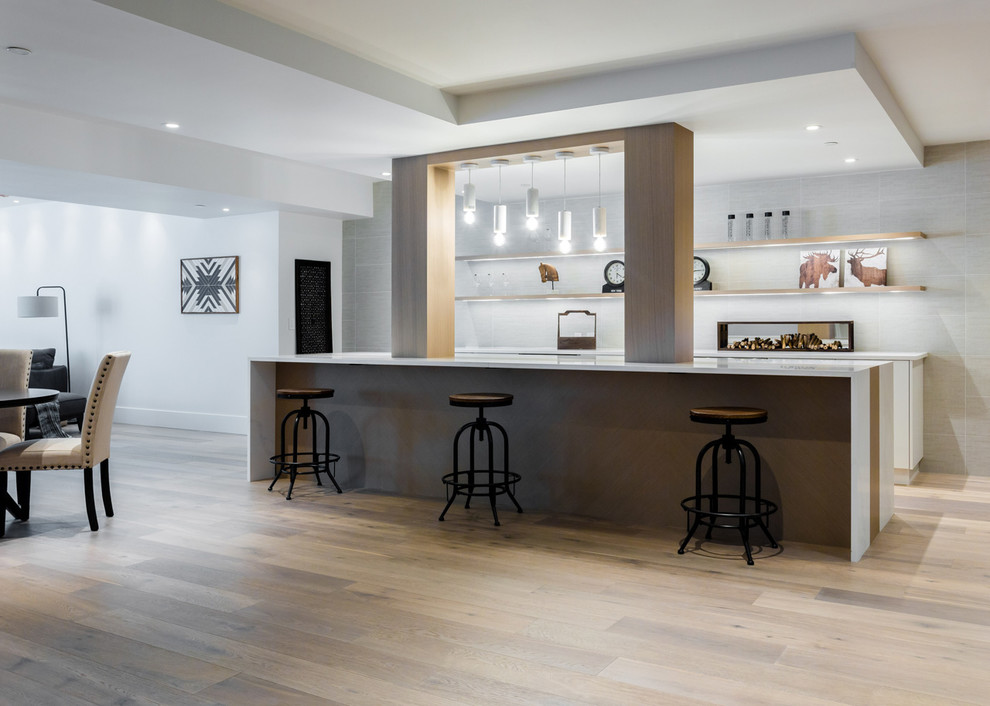 Design ideas for a large modern galley breakfast bar in Vancouver with a submerged sink, flat-panel cabinets, white cabinets, grey splashback, porcelain splashback, medium hardwood flooring, brown floors and white worktops.