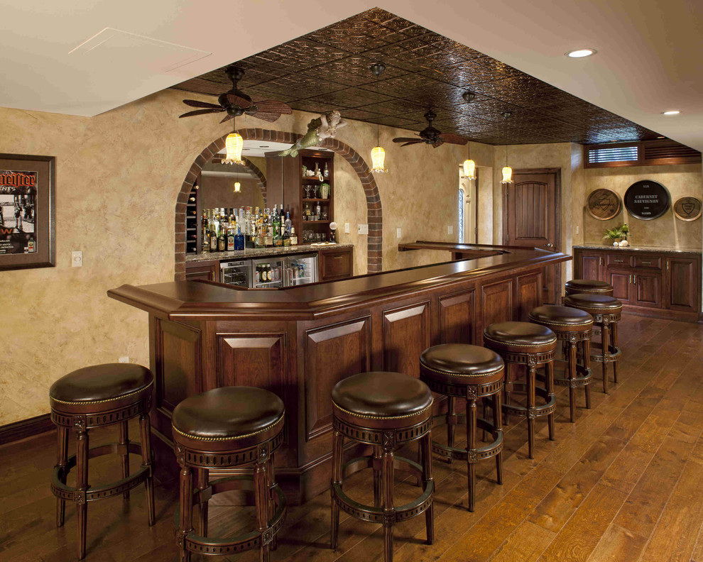 На фото: большой п-образный домашний бар в классическом стиле с барной стойкой, темным паркетным полом, фасадами с выступающей филенкой, темными деревянными фасадами, деревянной столешницей, зеркальным фартуком и коричневой столешницей