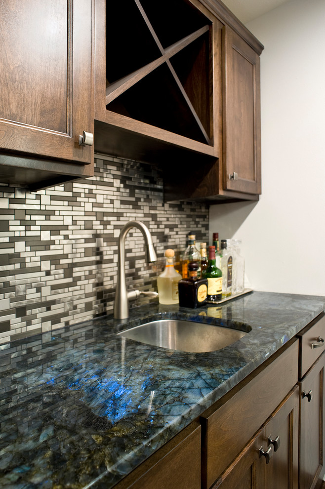 Photo of a traditional single-wall wet bar in Other with a submerged sink, raised-panel cabinets, brown cabinets, granite worktops, multi-coloured splashback and metal splashback.