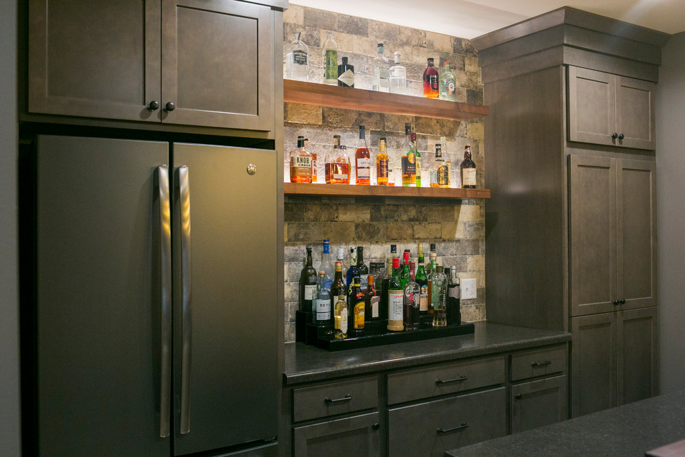 Example of a large arts and crafts galley light wood floor and beige floor seated home bar design in Other with a drop-in sink, recessed-panel cabinets, gray cabinets, solid surface countertops, gray backsplash, stone tile backsplash and gray countertops