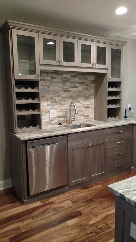 Example of a large transitional u-shaped light wood floor and brown floor wet bar design in Atlanta with a drop-in sink, glass-front cabinets, gray cabinets, granite countertops, beige backsplash, stone tile backsplash and gray countertops