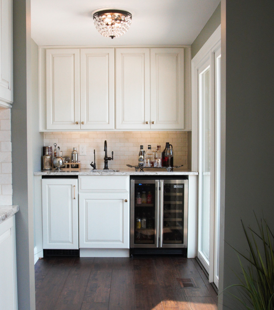 Exempel på en liten klassisk flerfärgade linjär flerfärgat hemmabar med vask, med en undermonterad diskho, luckor med upphöjd panel, vita skåp, bänkskiva i kvarts, vitt stänkskydd, stänkskydd i stenkakel och mörkt trägolv