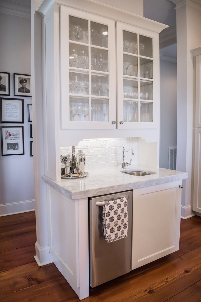 Bild på en vintage grå linjär grått hemmabar med vask, med en undermonterad diskho, luckor med glaspanel, vita skåp, granitbänkskiva, vitt stänkskydd, stänkskydd i tegel, mellanmörkt trägolv och brunt golv