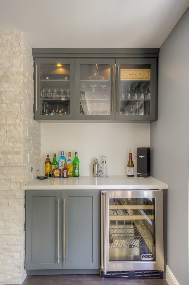 Idee per un piccolo angolo bar chic con ante in stile shaker, ante grigie, pavimento in legno massello medio e top bianco