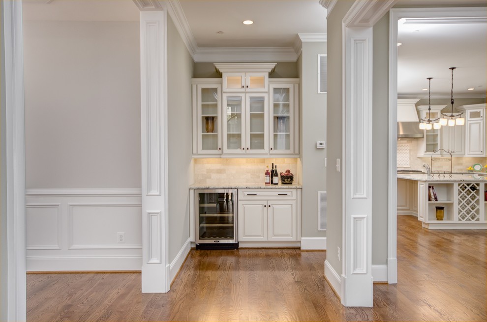 Inspiration for a small timeless single-wall medium tone wood floor home bar remodel in DC Metro with raised-panel cabinets, beige cabinets, granite countertops, beige backsplash and travertine backsplash