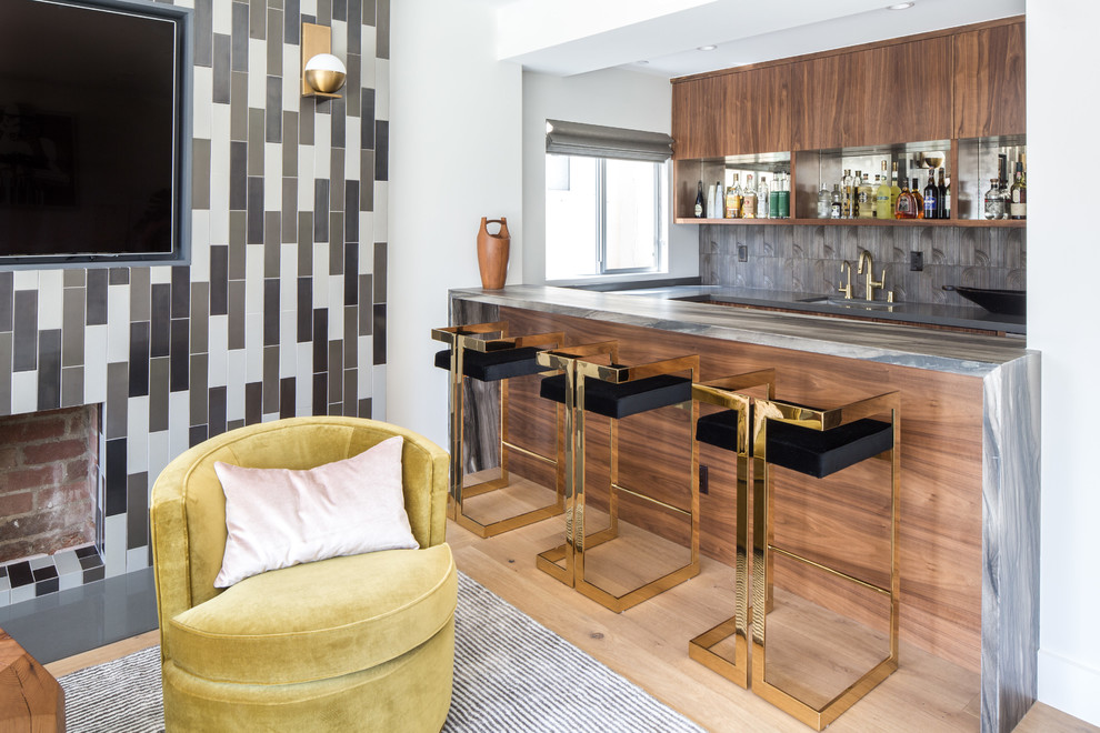 Cette image montre un bar de salon parallèle design en bois brun avec des tabourets, un évier encastré, un placard à porte plane, une crédence grise, parquet clair, un sol beige et un plan de travail gris.