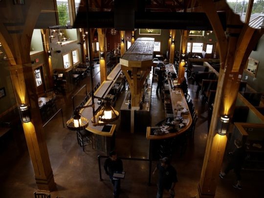 Cette photo montre un très grand bar de salon montagne en U avec des tabourets, un plan de travail en inox et sol en béton ciré.