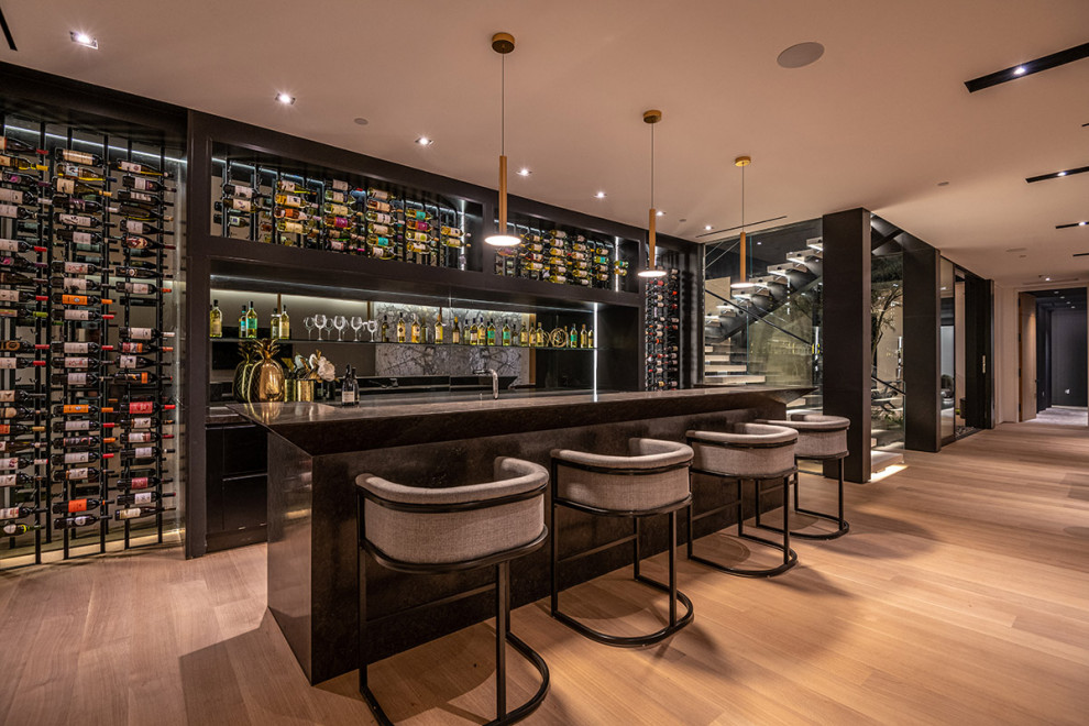Exemple d'un bar de salon avec évier tendance avec un placard à porte plane, des portes de placard noires, une crédence miroir, un sol en bois brun, un sol marron et plan de travail noir.