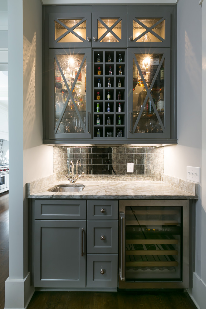 Coastal single-wall wet bar in Charleston with a submerged sink, glass-front cabinets, grey cabinets, metal splashback, dark hardwood flooring, brown floors and beige worktops.