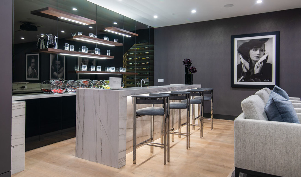 Cette image montre un bar de salon parallèle design avec des tabourets, un placard à porte plane, des portes de placard noires, une crédence grise, une crédence miroir, parquet clair, un sol beige et un plan de travail blanc.
