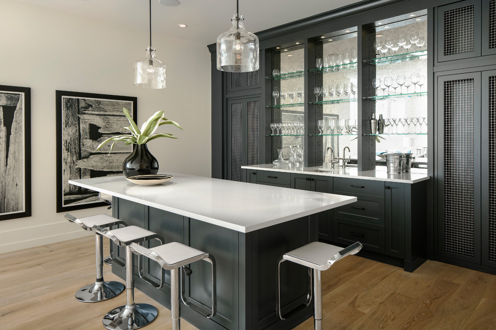This is an example of a classic galley breakfast bar in Calgary with a submerged sink, recessed-panel cabinets, black cabinets, engineered stone countertops, glass sheet splashback, light hardwood flooring and grey worktops.