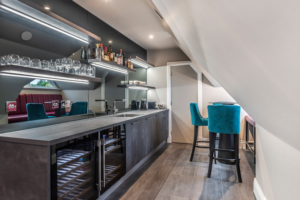 This is an example of a contemporary single-wall wet bar in Berkshire with a built-in sink, flat-panel cabinets, grey cabinets, mirror splashback, medium hardwood flooring, brown floors and grey worktops.