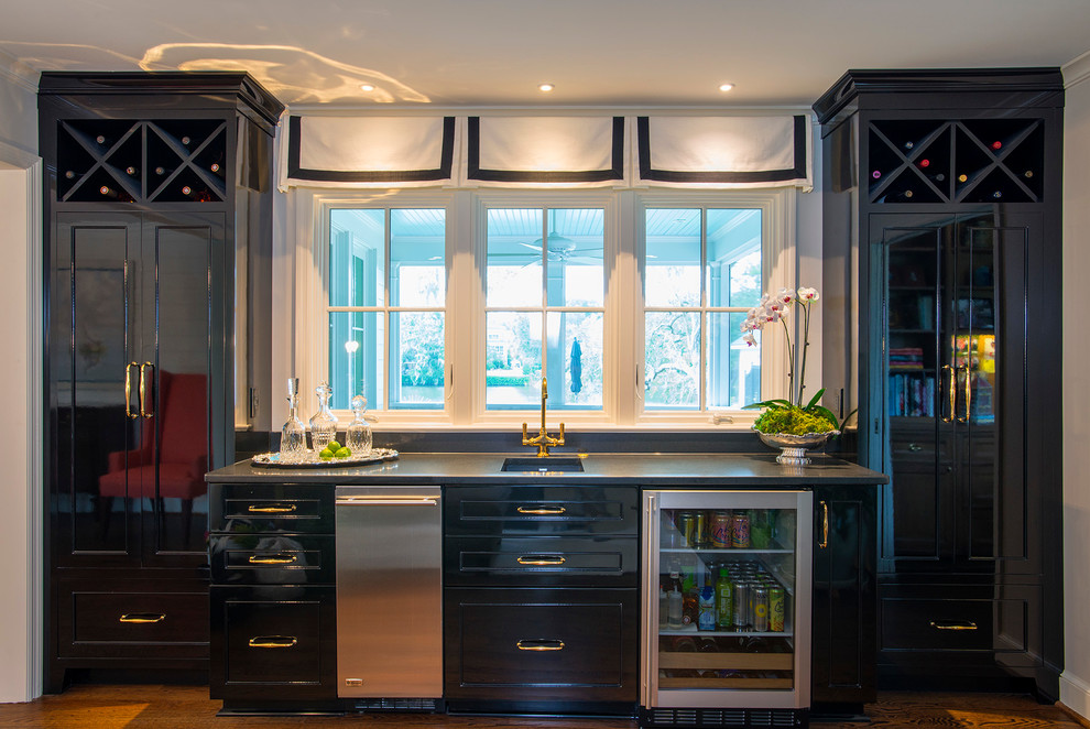 Inspiration for a mid-sized transitional single-wall medium tone wood floor and brown floor wet bar remodel in Charleston with an undermount sink, recessed-panel cabinets, black cabinets, granite countertops, black backsplash and stone slab backsplash