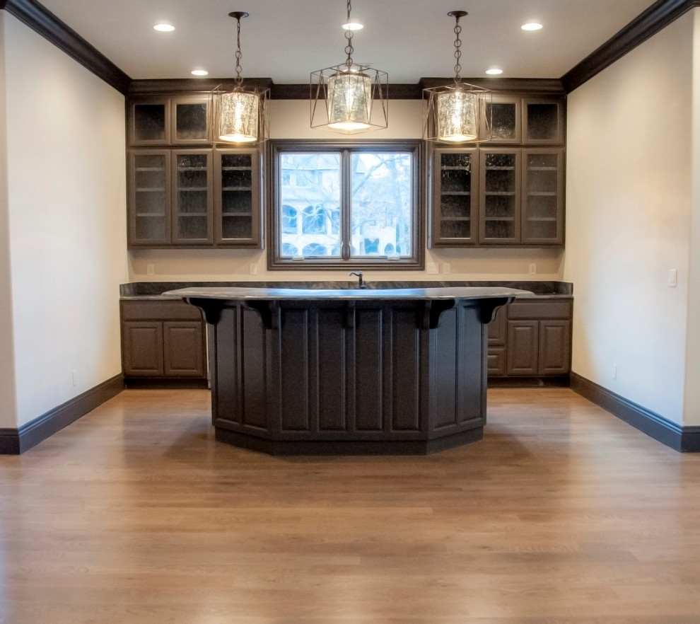 Large transitional l-shaped medium tone wood floor seated home bar photo in Other with an undermount sink, glass-front cabinets, dark wood cabinets and granite countertops