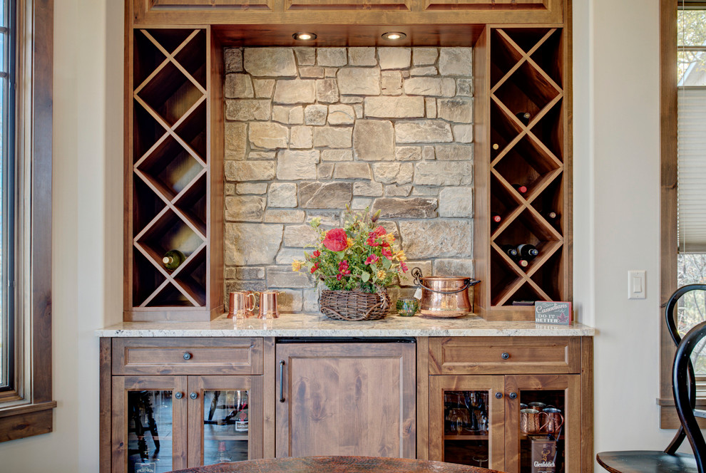 This is an example of a medium sized rustic single-wall home bar in Calgary with glass-front cabinets, medium wood cabinets, granite worktops, beige splashback and stone tiled splashback.