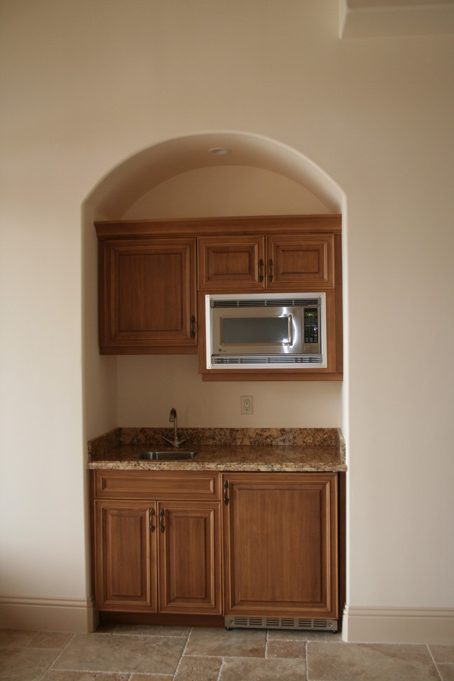 Cette image montre un petit bar de salon avec évier linéaire traditionnel en bois brun avec un évier encastré, un placard avec porte à panneau surélevé, un plan de travail en granite et un sol en travertin.