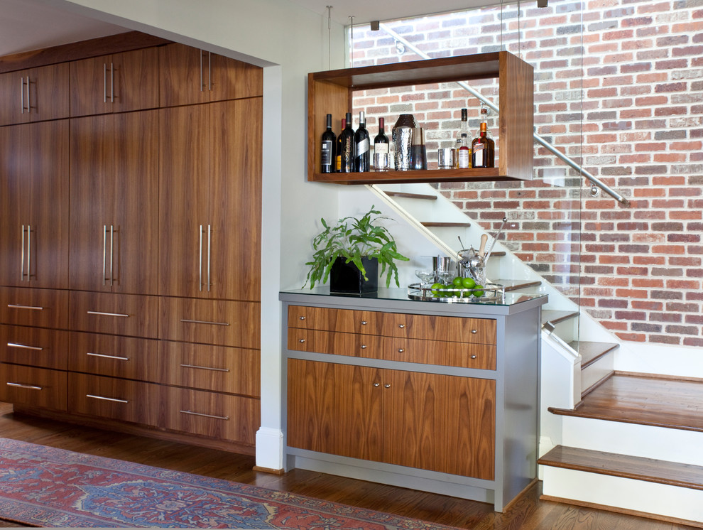 Aménagement d'un bar de salon linéaire classique en bois brun avec aucun évier ou lavabo, un placard à porte plane, une crédence en feuille de verre et un sol en bois brun.