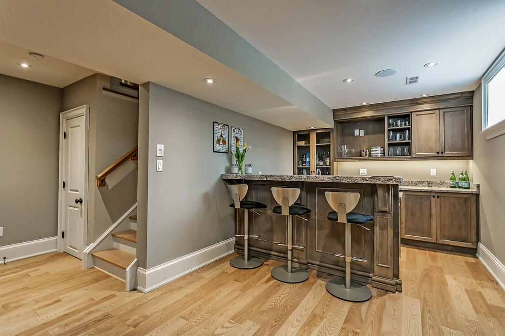 Foto de bar en casa con barra de bar de galera tradicional renovado de tamaño medio con armarios estilo shaker, puertas de armario de madera oscura, suelo de madera clara, encimera de granito y suelo beige