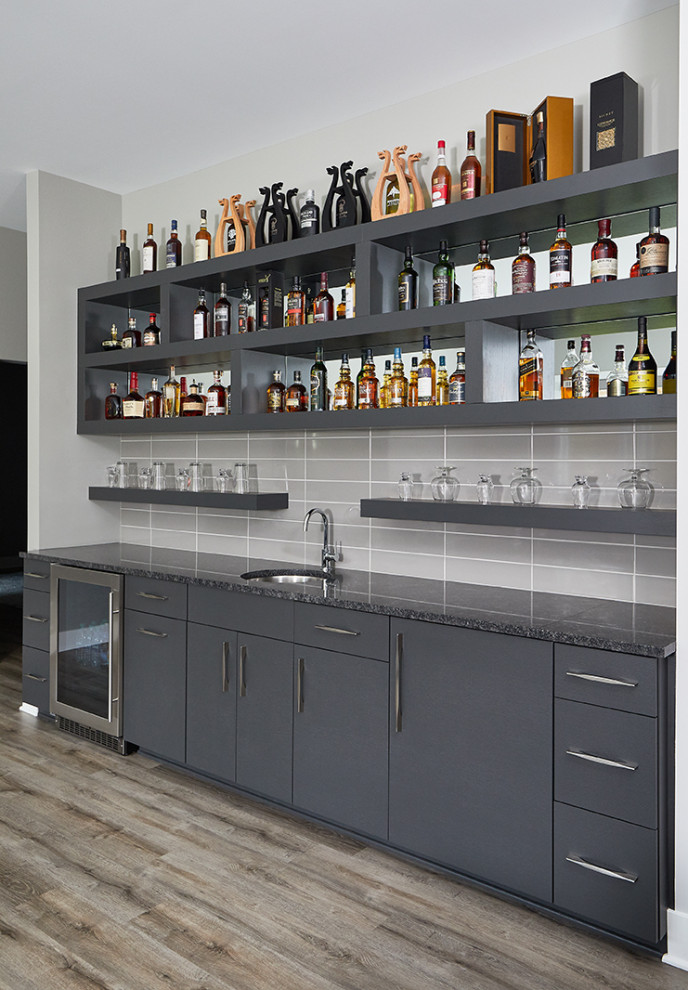 Cette image montre un bar de salon avec évier linéaire traditionnel en bois foncé avec un évier encastré, un placard à porte plane, un plan de travail en granite, une crédence grise, une crédence en céramique, un sol en bois brun, un sol gris et plan de travail noir.