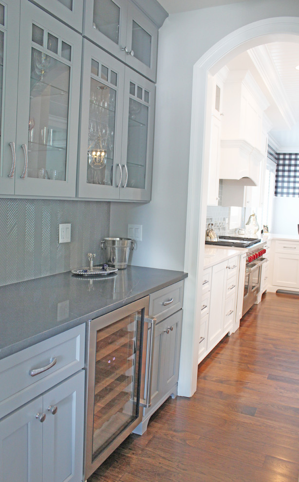 Inredning av en modern liten grå linjär grått hemmabar med vask, med grå skåp, grått stänkskydd, mellanmörkt trägolv, brunt golv, bänkskiva i kvarts och luckor med infälld panel