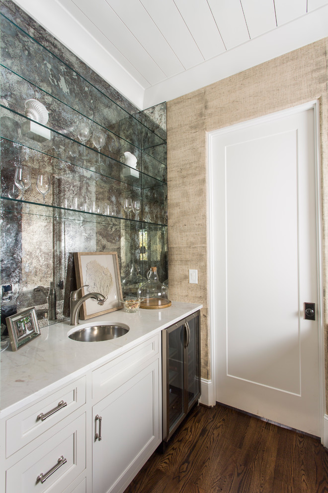 Bild på en liten tropisk parallell hemmabar med vask, med en undermonterad diskho, luckor med profilerade fronter, vita skåp, marmorbänkskiva, grått stänkskydd, spegel som stänkskydd, mörkt trägolv och brunt golv