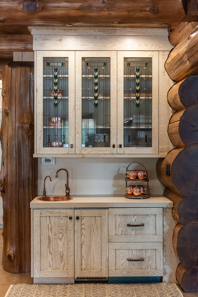 Imagen de bar en casa con fregadero lineal rústico con fregadero encastrado, armarios tipo vitrina, puertas de armario de madera clara, salpicadero beige y encimeras beige