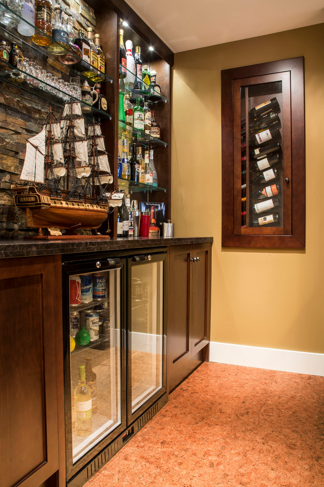 This is an example of a medium sized classic single-wall wet bar in Calgary with recessed-panel cabinets, dark wood cabinets, granite worktops, brown splashback, stone tiled splashback, cork flooring, brown floors and black worktops.