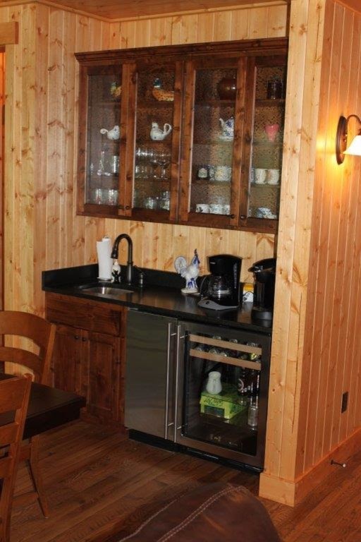 Exempel på en liten rustik linjär hemmabar med vask, med en undermonterad diskho, luckor med glaspanel, skåp i mellenmörkt trä, brunt stänkskydd, stänkskydd i trä, mellanmörkt trägolv och brunt golv