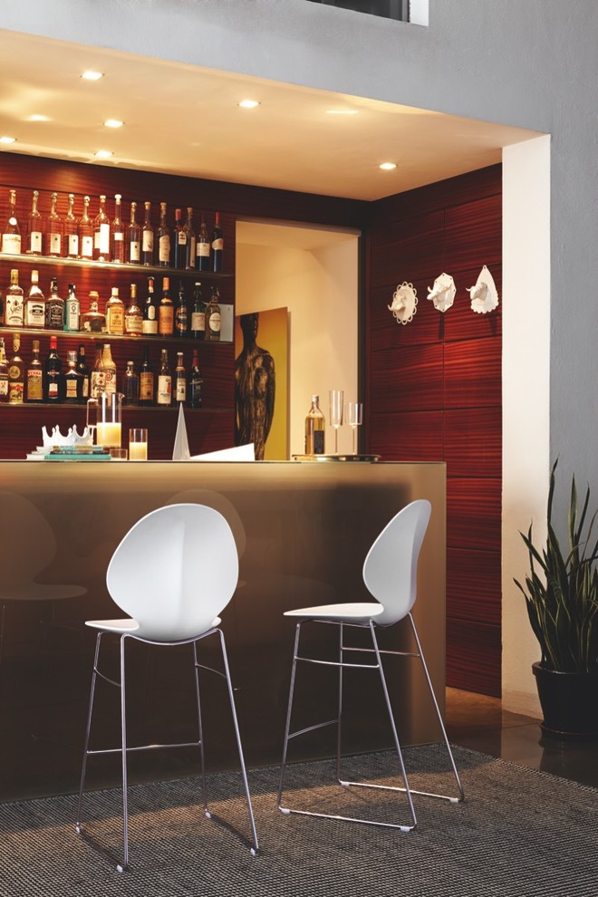 Immagine di un bancone bar minimal di medie dimensioni con ante marroni, top in vetro, paraspruzzi marrone e pavimento in cemento
