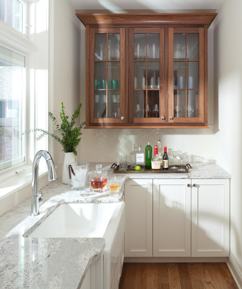 Wet bar - mid-sized transitional l-shaped medium tone wood floor wet bar idea in New York with an undermount sink, shaker cabinets, white cabinets, marble countertops, white backsplash and subway tile backsplash