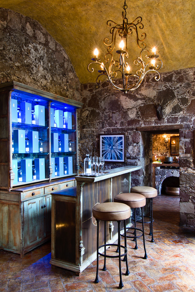 Cette image montre un bar de salon méditerranéen en bois vieilli avec des tabourets, un placard sans porte, un plan de travail en bois et un sol en brique.