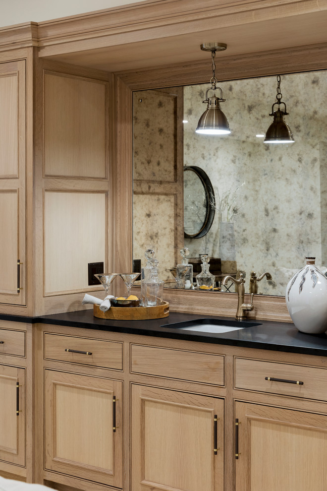 Medium sized traditional galley wet bar in Minneapolis with a built-in sink, beaded cabinets, light wood cabinets, soapstone worktops, brown splashback, wood splashback, carpet, beige floors and black worktops.